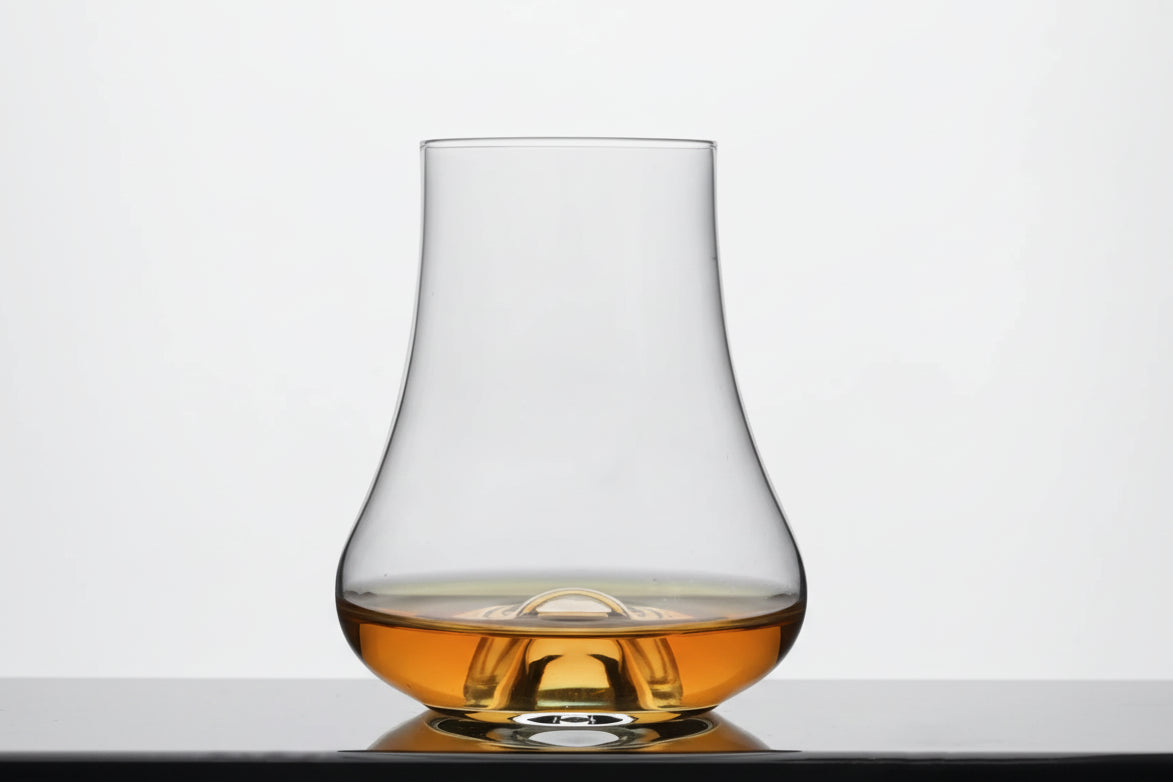 Clear glass tequila glass with amber liquid on a light gray background